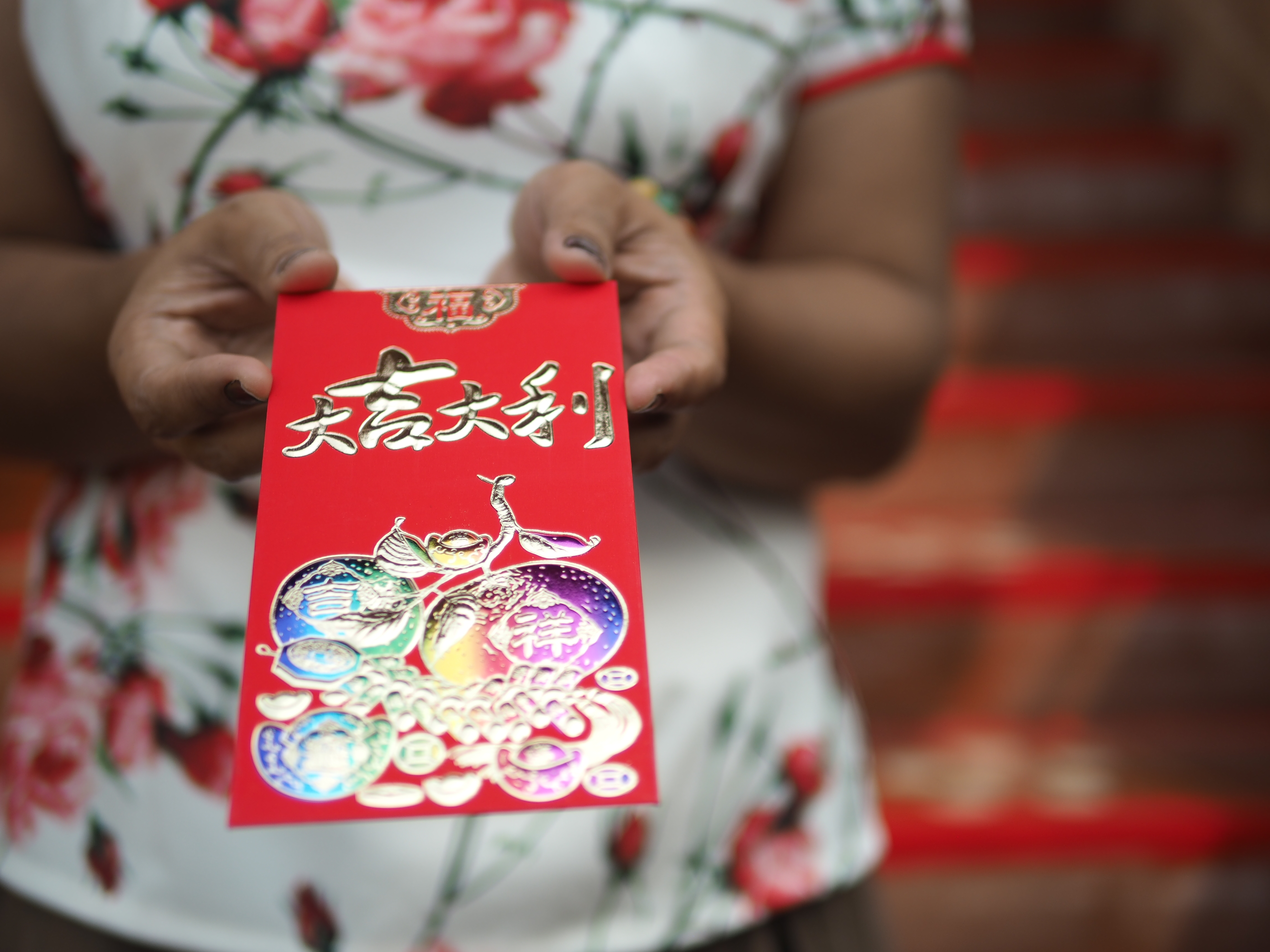 Woman in a qipao holding out a red envelope with both hands.
