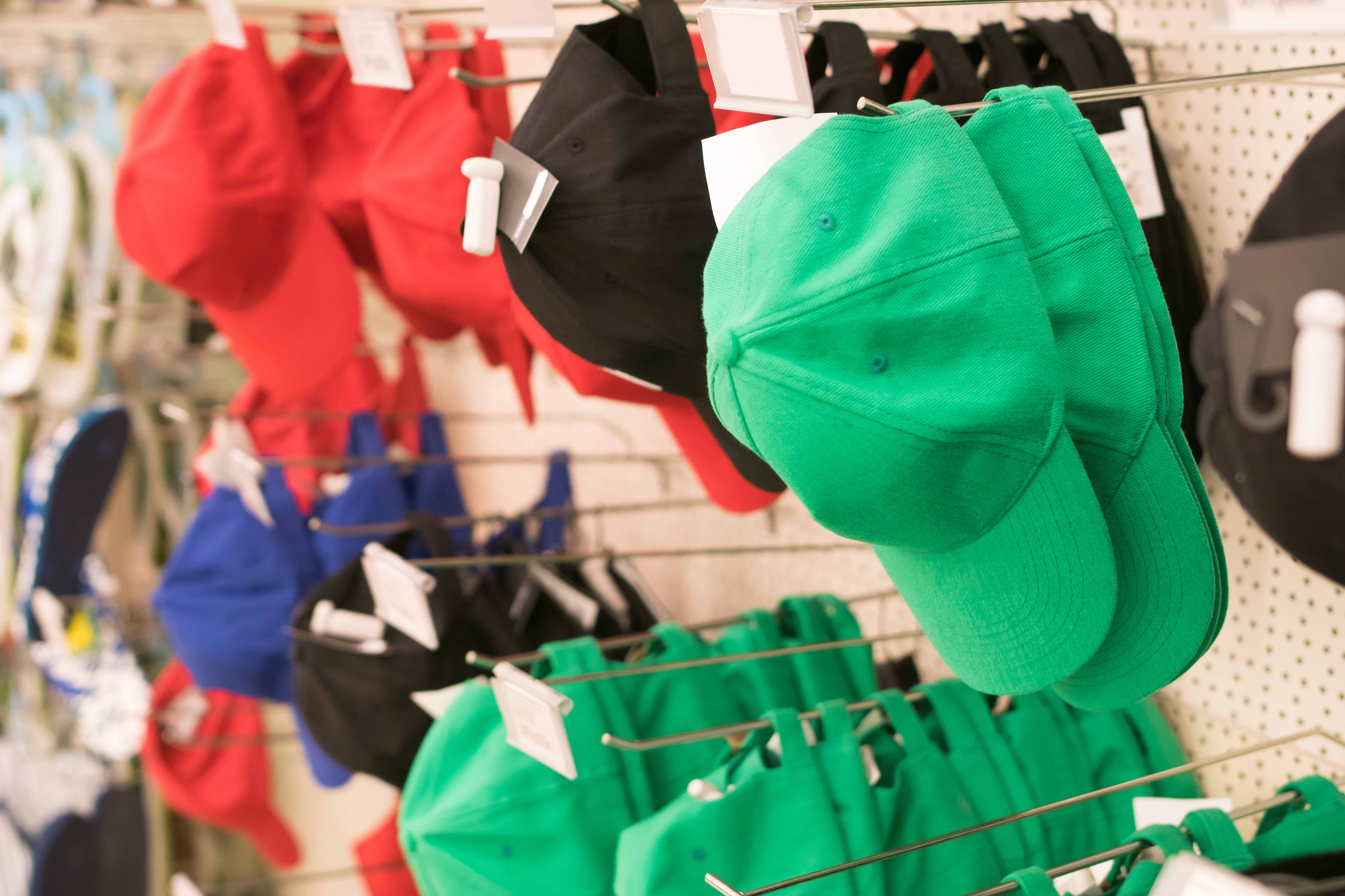 Green, red, and black baseball caps hanging on hooks against a white wall.