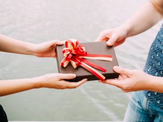 Two people exchange a gift wrapped in brown paper using both hands